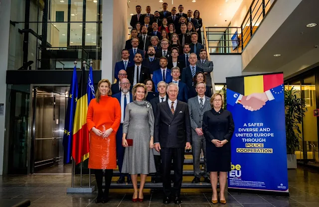 Queen Mathilde wears a black and white checked dress, with a wine-red cape coat by Natan. Diamond parrots brooch