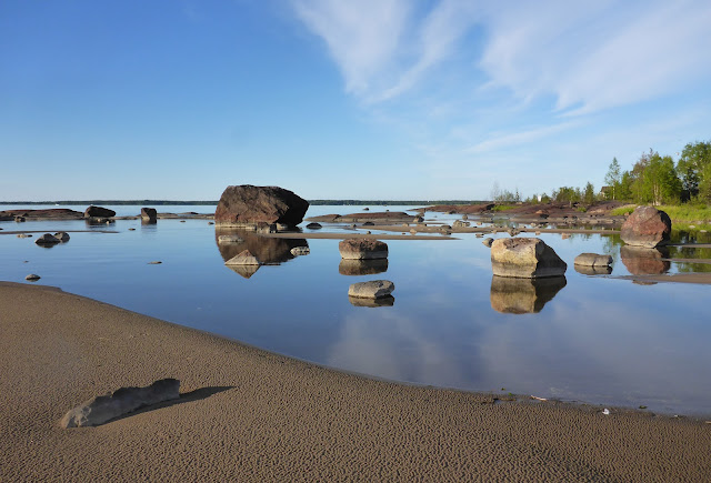 Matala hiekkaranta ja lohkareita, peilityyni vesi