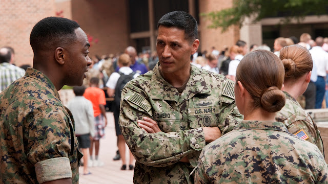 Three individuals in military camo talking in a courtyard