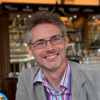 photo of a man with glasses in a bar smiling.