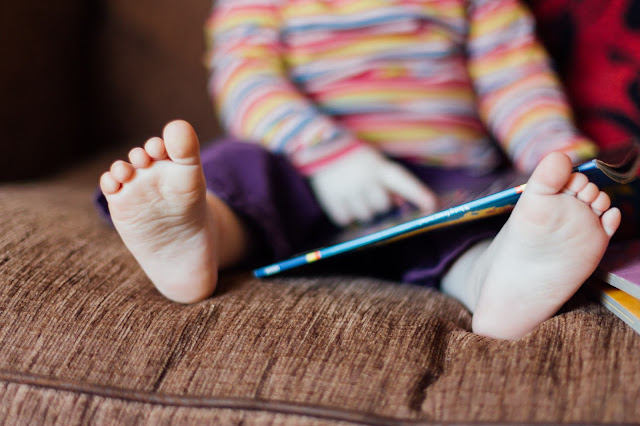 Shot of a child's feet with a book nearby as they sit on a sofa