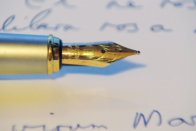 Pluma de escribir dorada sobre una hoja de papel blanco con algunas letras