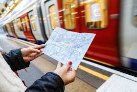 Pic of lady's hands holding small London tube map on platform as tube passes