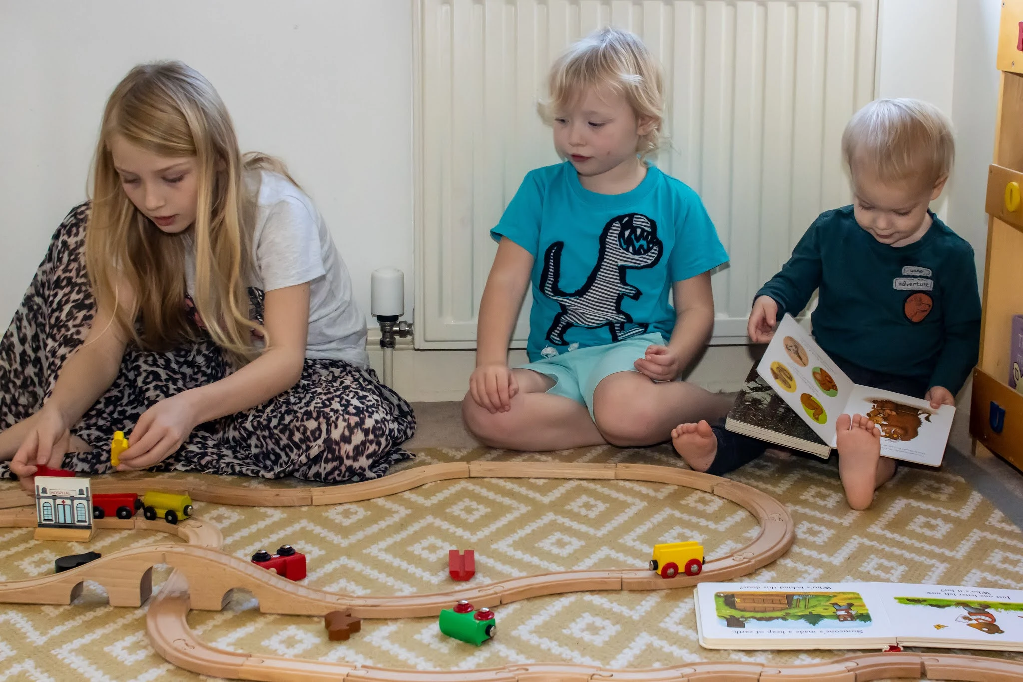 3 children playing in front of a radiator with a hive heating thermostat valve, 2 are playing with a wooden train track and one is reading a book