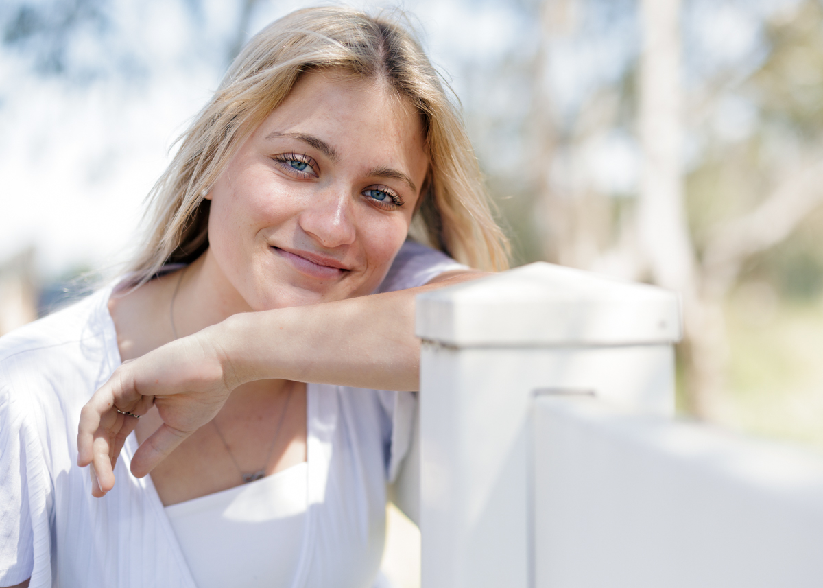 High school senior girl leaning on white fence