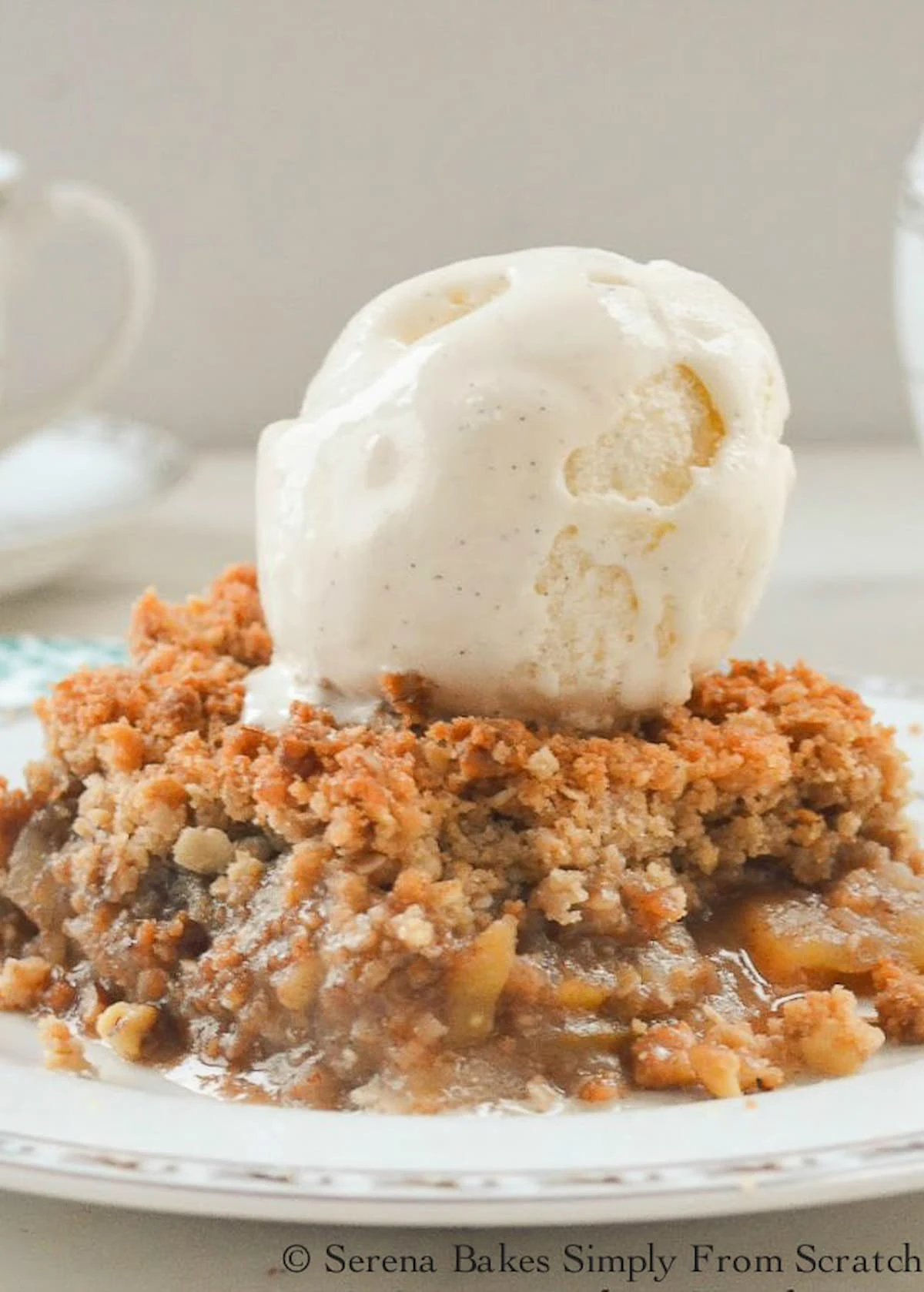 A side shot of Apple Crisp on a white plate topped with Vanilla Ice Cream.