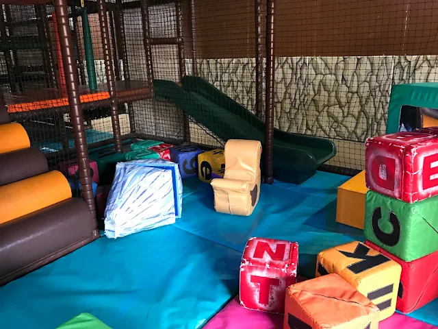 A view of the toddler soft play area including large cubes with letters on, a slide and a raised platform