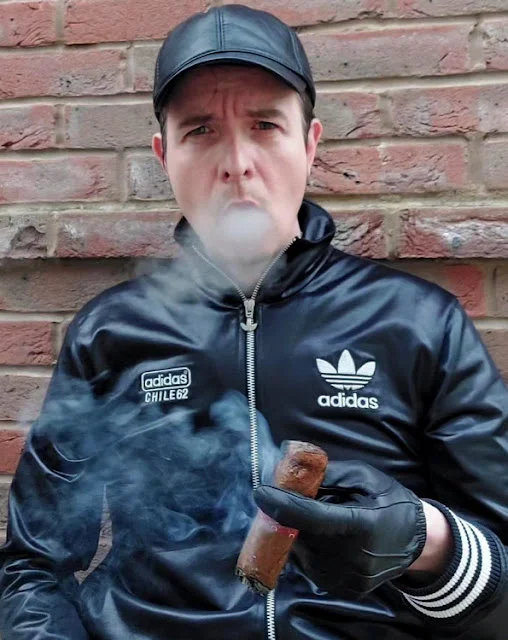 Master Rian wearing leather tracksuit with gloves and hat smoking cigar