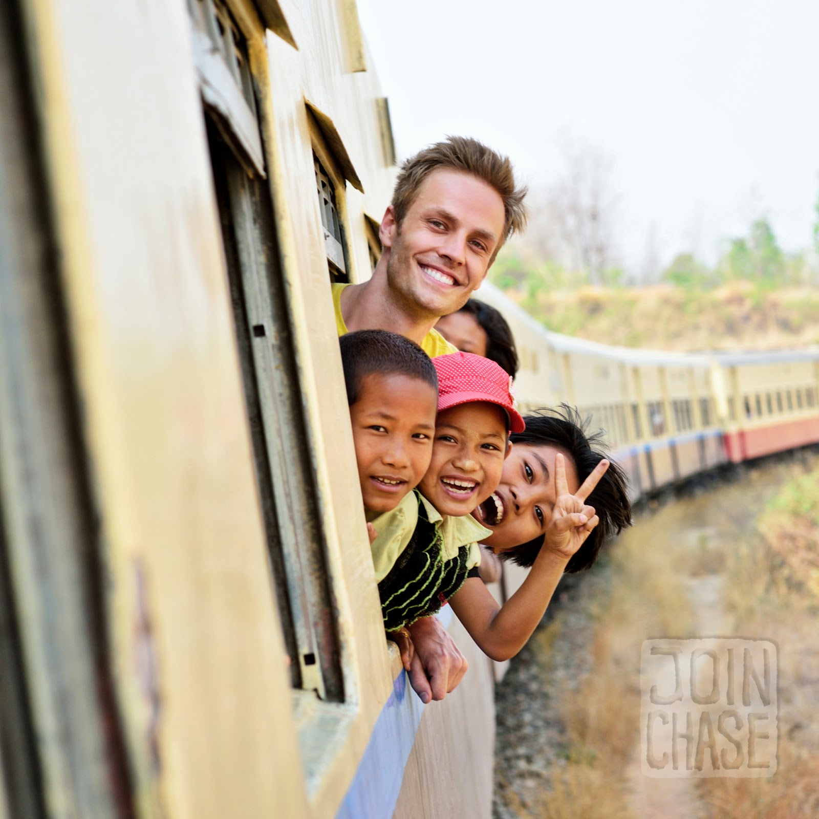 Chase Chisholm peeking out the window with children on a train from Yangon to Bagan, Myanmar.