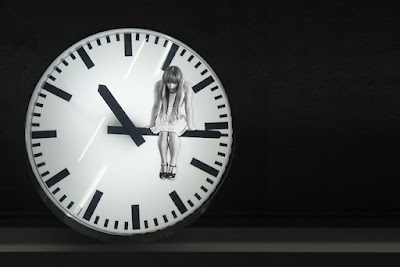 An image of a girl in white dress sitting on the hands of clock and looking down- sad girl dp