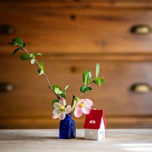 tiny paper house displayed on flat surface next to small flower arrangement in blue bottle
