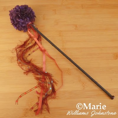 Black wood stick topped with purple material and ribbons