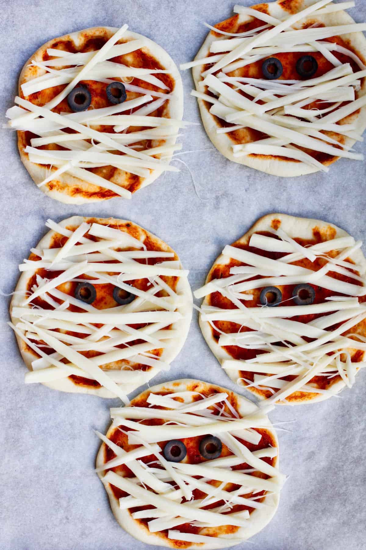 Mini Pizza Mummies assembled with cheese and olives before baking.