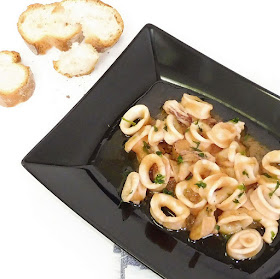 Plato de cazuela de calamares a la cerveza con trozos de pan sobre fondo blanco