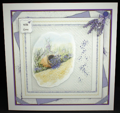 Image is a photo of a handcrafted card, featuring many layers, decoupage, and a watercolour cascade of lavender.