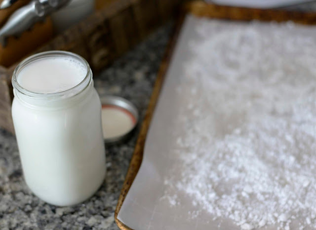 coconut milk in a mason jar with pulp sitting on a parchment paper lined baking sheet on a grey granite countertop