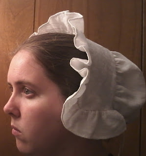 The author, wesring a white linen cap reaching just below the ears, the front and  side edges finished with a 2 inch ruffle of the same linen.