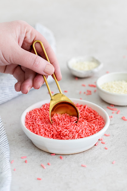 hand scooping sprinkles with a gold spoon.