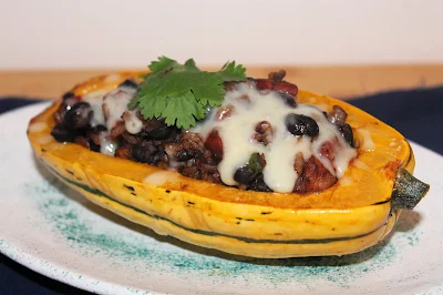 Serving plate of a chorizo and black bean stuffed delicata squash half.