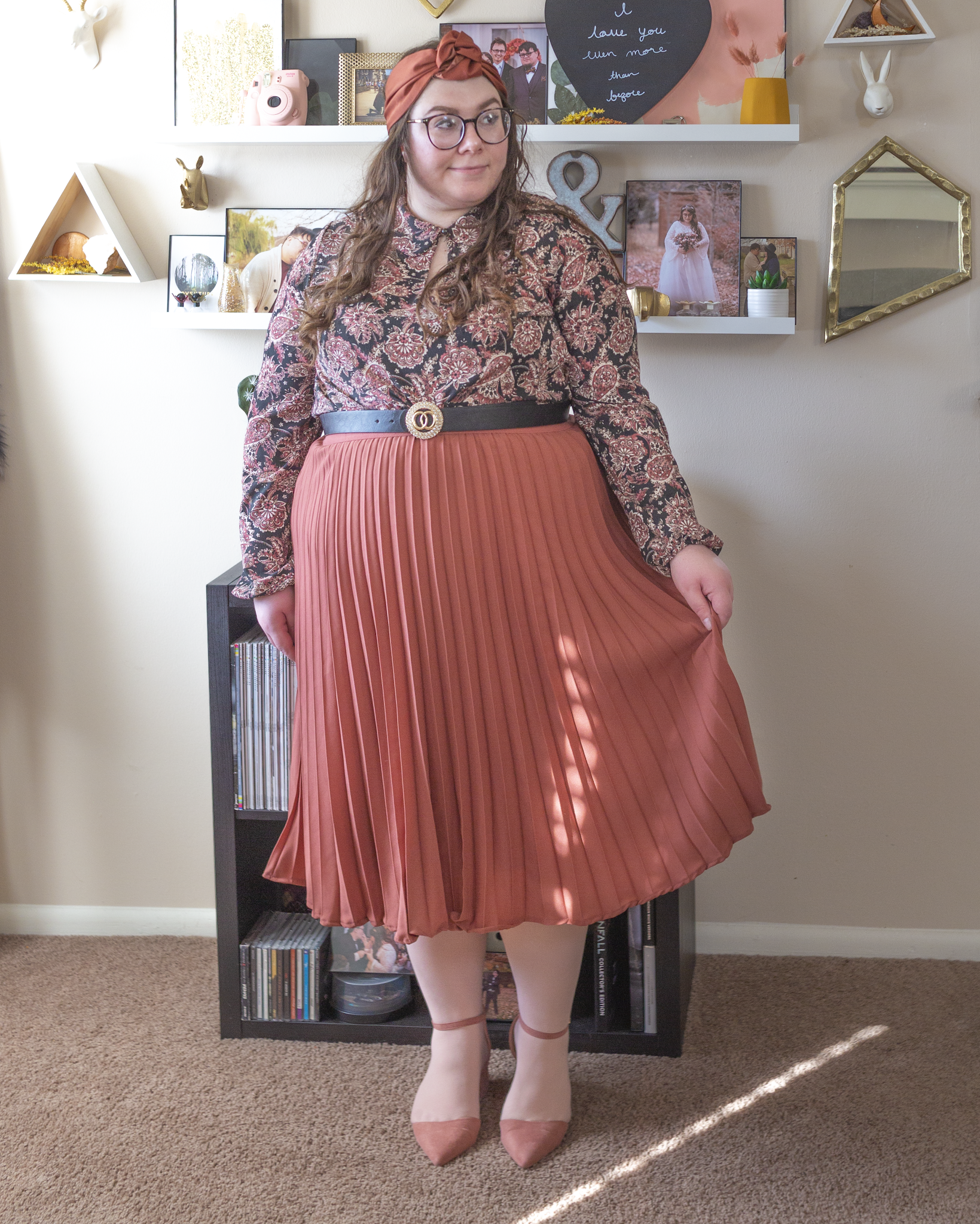 An outfit consisting of a rose colors headband, a black and pink paisley print peter pan collared dress with a keyhole neckline worn as a top under a rose colored pleated midi skirt, pastel pink tights and pastel pink suede ankle strap pointed toe heels.