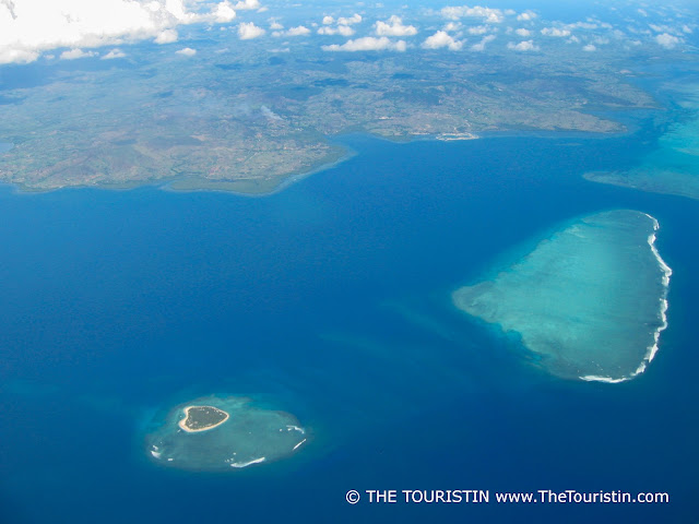 Reefs and sand-fringed islands in the midst of a turquoise blue sea under a slightly cloudy sky.