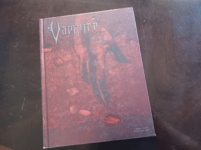 photo of the red cover of Vampire: the Requiem-- title in spiky letters, glossy rose petals strewn across over the image of a limp hand