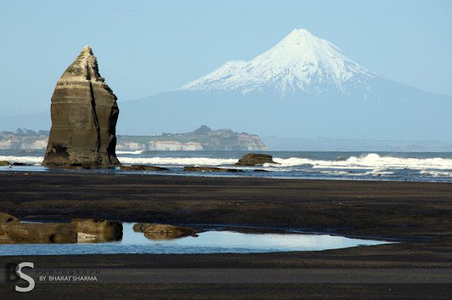 After wonderful Photo Journeys like 'Breathtaking helicopter flights exposing the magnificent views of the pristine alpine environment in the AorakiMount Cook World Heritage Park - By BHARAT SHARMA' and 'Bay Of Islands', here is another one from Mount Taranaki, which is again one of the main places in New Zealand to visit. Let's check out this lastest Photo Journey from Bharat's Travelling Camera...Mount Taranaki or Mount Egmont is an active but quiescent strato volcano in the Taranaki region of west coast of New Zealand's North Island. Although the mountain is more commonly referred to as Taranaki it has two names under the alternative names policy of the New Zealand Geographic Board.The 2520 meters high mountain is one of the most symmetrical volcanic cones in the world. There is a secondary cone.... Because of its resemblance to Mount Fuji, Taranaki provided the backdrop for the movie The Last Samurai. (Courtney - http://en.wikipedia.org/wiki/Mount_Taranaki)Here is a link which tells very well about the activities one can plan while in Mount Tarnaki - http://www.taranaki.info/visit/content.php/page/taranaki-s-top-50-must-do-experiencesThis mountain is a source of more than 49 rivers and water-streams...It's a botanically unique area containing a wide variety of vegetation from sub-tropical semi-coastal forests in the Kaitake Ranges through to sub-alpine herb fields...Many bird species can also be found in the forests surrounding the mountain...Taranaki issues a challenge that some who are tempted to climb... In summers, a climb to the summit requires a day approximately... and a good level of fitness is something that is required... However, the mountain sits close to the Tasman Sea and is subject to rapid and violent weather changes. Many who attempt the climb are less than adequately equipped. A combination of these factors has meant that Egmont has seen more climbing fatalities than any other mountain in New Zealand. (For more in this regard, check out http://www.summitpost.org/mt-egmont-taranaki/152168A wonderful view of Mount Taranaki through huge sea which looks very small as compared to this Mountain !!!Here is one of the drmamatic photograph of Mount Taranaki, which is clicked from a plane. Whole area is covered by dense clouds and peak of Mount Taranaki is visible with snow cap on it. Check out http://www.flickr.com/photos/timboss81/6352143584/While reading more on internet about Mount Taranaki, we found another cool article describing various places to stay in Taranaki region with some decent options for climbers and botany lovers. Check out http://www.newzealand.com/int/article/national-parks-egmont/ for more details.A shot take on sea side... Stone standing out brilliantly through curved sand...Water movement over this sand has given it a dramatic texture and helped in overall composition of this photograph...There are three roads leading part-way up the mountain. The highest is to East Egmont plateau, with a viewing platform and parking facilities for the ski-field. It lies at the transition between sub-alpine scrub and alpine herb fields.Here ends the journey to Mount Taranaki by Bharat Sharma