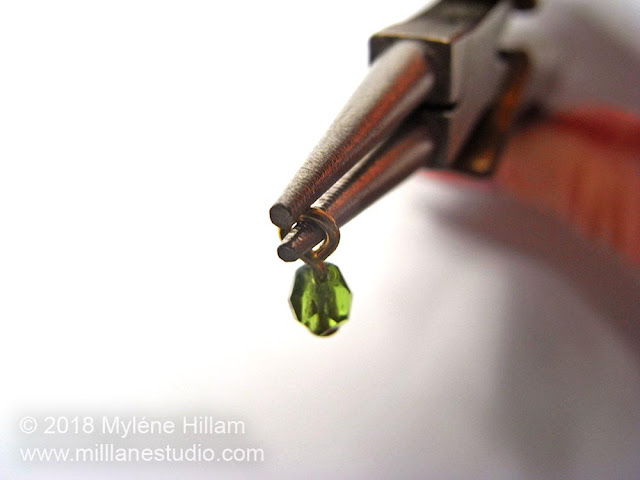 Forming a simple loop on an olivine bead dangle using round nose pliers.