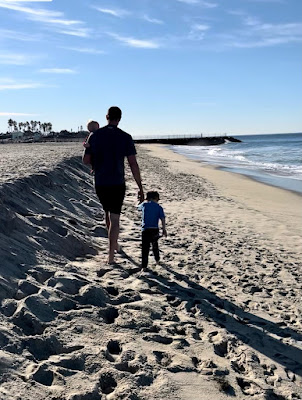 father walking with two kids on the beach