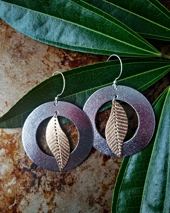 Metallic silver and gold tone earrings featuring a leaf shape overlapping a doughnut shape.