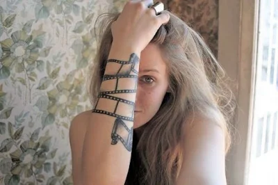 Chica rubia con tatuaje de un film de pelicula a modo de brazalete