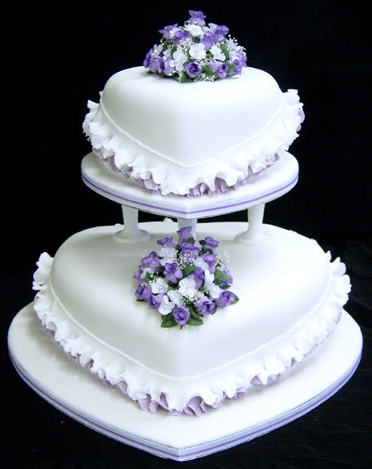 White heart shaped wedding cake with purple trimming and small purple and 