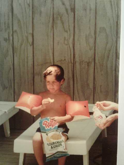 In a family photograph, Greig Roselli eats potato chips and wears floaties at the beach.