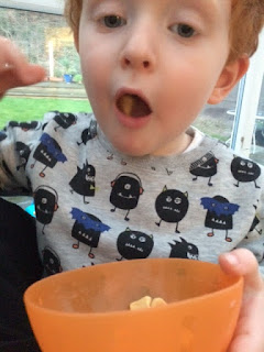 Red haired toddler with a bowl full of snacks and one in his mouth!