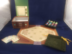 The components of War Chest. A game board, with several cards arrayed to one side, the velvet bags on the other side, a tray of tokens behind it, and the game box lying open nearby.