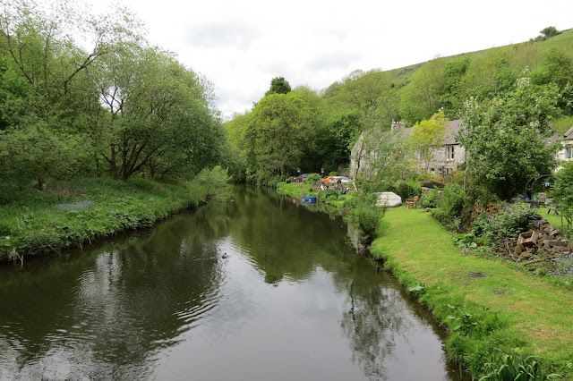 Looking along the river, a grassy embankment and cottages by the side of the water.