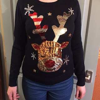 A navy jumper featuring a sequined rudolph with closed eyes. Rudolph's antlers are made with two sided sequins; brushed one way, the antlers are gold, brushed the other, the antlers are stripped white and red. To show in this photo, one antler is one red and white and the other is gold.