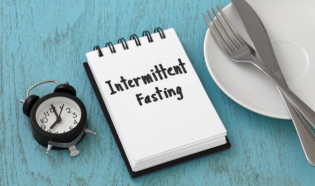 A notebook with 'Intermittent Fasting' written on it, next to a plate and utensils, depicting the concept of time-restricted eating for potential fat loss in women.