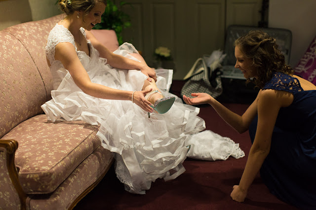 On the morning of July 8th, the rainclouds were threatening to unleash their fury, but it didn’t matter because this was Anna and Ben’s wedding day, and for that reason alone, this day would sparkle! From the moment we got to the church, activities were in full gear…fun and impromptu pictures of the bride with her bridesmaids, as they assisted Anna  into a wedding dress that was seemingly made for her…a mermaid-shaped, intricately laced, floor length, white  gown, with a scalloped V-neck front, and a diamond-shaped, cut-out in the back.  An embroidered handkerchief was tucked inside her garter as a “remembrance” of her grandmother.  The six bridesmaids wore individually designed, royal blue chiffon gowns, and each carried a similar version of Anna’s lush bouquet of pale, ivory roses and white lilies.   Impromptu shots of the relaxed and charismatic groom with his groomsmen came next.  The comradery they share was evident in every photograph!  Then it was time to squeeze in a sentimental “first look” for the bride’s dad before the romantic “first look” with the groom, and you can tell from the expression on Ben’s face…and the height of his jump…how excited he was to finally see her!    The First United Methodist Church of Oklahoma City was an ideal location for this couple’s wedding.  Located in the heart of OKC, its ministry began during the land run of 1889, and has continued to share the gospel through two wars and the infamous April 1995 bombing.  The large, stained glass windows, dark mahogany wood, and simple, yet elegant sanctuary was the perfect backdrop for these two young people who were meant for each other.    When asked what the best part of the day was, Anna said, “getting to see Ben for the first look, and his reaction to seeing me.”  Ben’s response was “getting to see Anna walk down the aisle and say our vows to each other.”    Anna felt that her wedding day went smoothly, but if she were to do it over again, she would hire a wedding planner and a florist to take some of the responsibility off herself, family, and friends.  Her favorite piece of advice to a prospective bride and groom:  “When things get stressful or overwhelming—and at some point they will—just take a break, step back, and enjoy.”  After the couple exchanged vows, guests were invited to participate in a fun, romantic, and lively reception that included the “first dance,” dances with the parents, toasts to the bride and groom, a sit-down dinner, the cake cutting, throwing of the bouquet and garter…and lots and lots of dancing!  At the end of the evening, it was time for friends and family to gather together and wish this fun-loving couple farewell and best wishes for a wonderful life together!