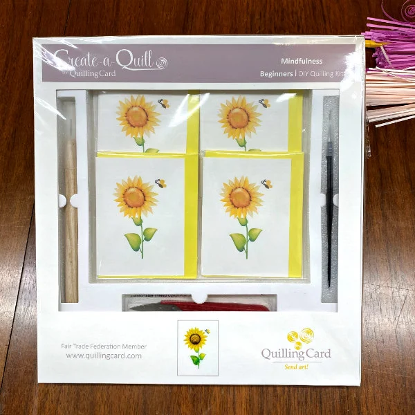 Quilling Card Sunflower Kit in clear plastic package on wood table with batch of quilling paper strips