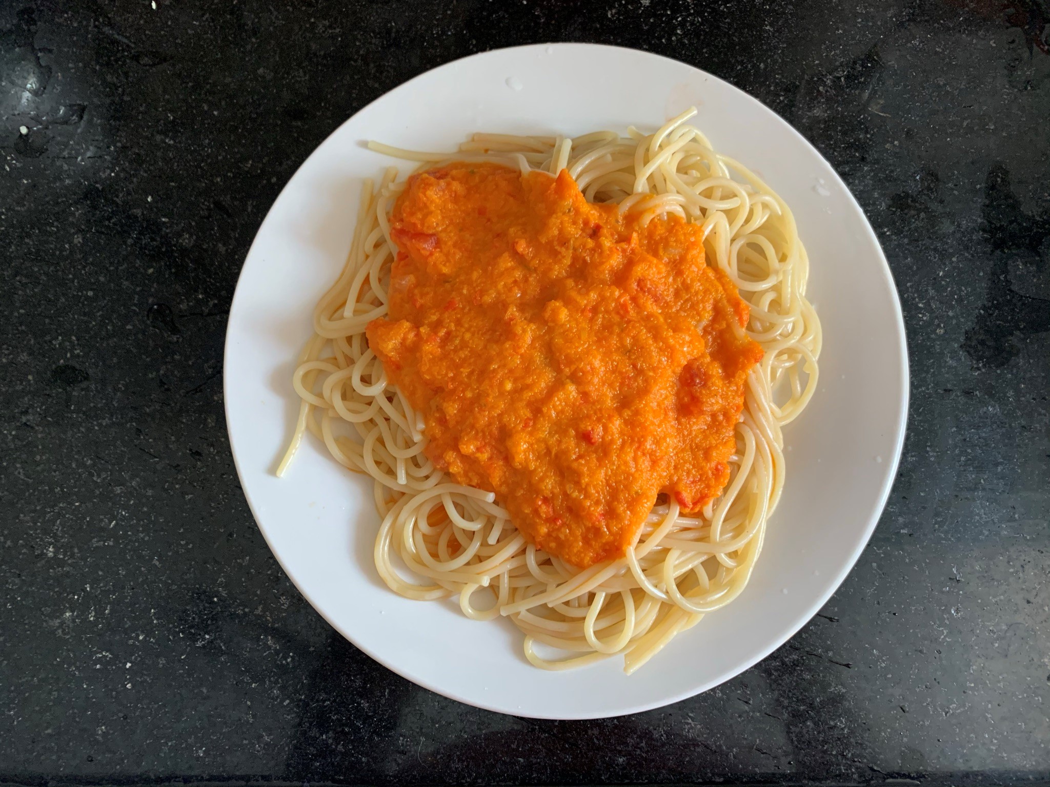 Foto de prato branco com espaguete e o molho caseiro de tomates para massas por cima. Prato sob mármore preto.