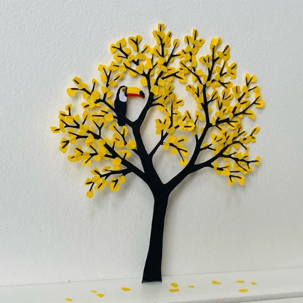 miniature papercut tree with yellow leaves and toucan with colorful beak sitting on a branch