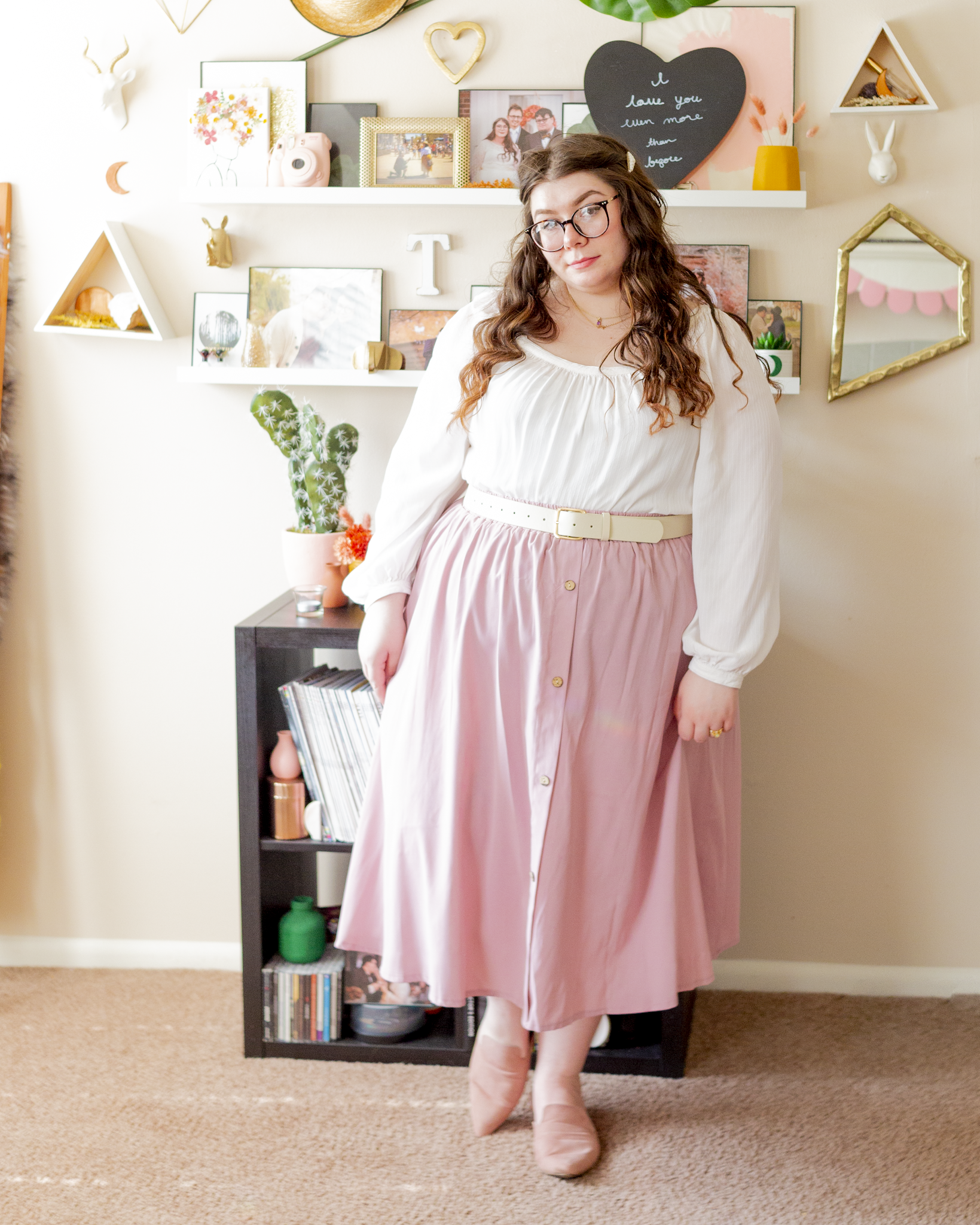 An outfit consisting of a white square neck long sleeve cotton blouse tucked into a pastel pink button up midi skirt and pastel pink suede mules.