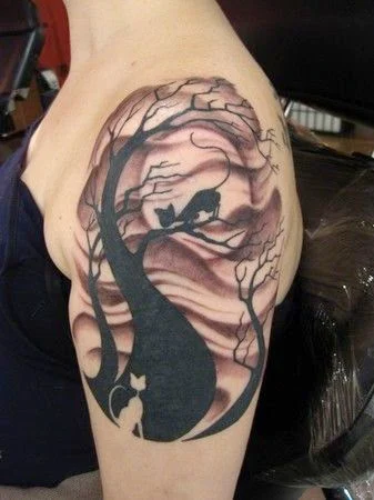 precioso tatuaje en el hombro de una chica, el tatuaje es de un gato subido en un arbol el fondo de noche con nuves en grises