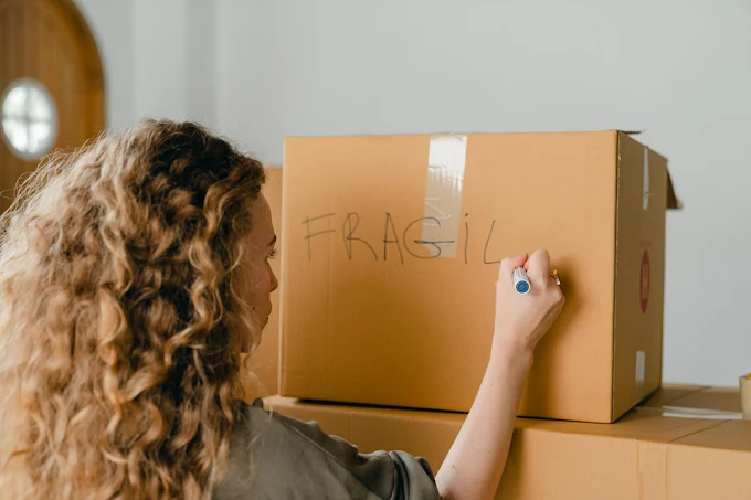 Mulher escrevendo FRÁGIL numa caixa de mudança