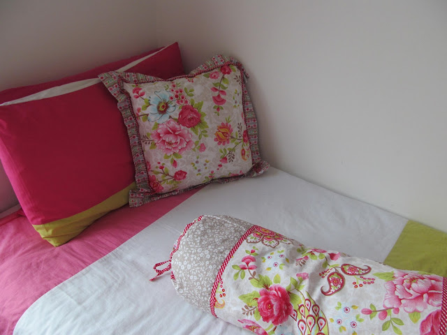 square floral cushion on block pink and green and white bedding with long matching floral cushion just coming into foreground of shot