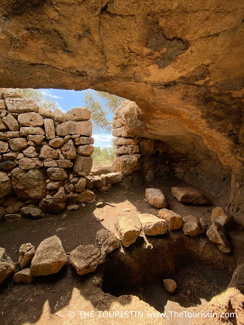 A cave behind a tall dry stone wall.