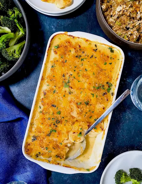 Top view of potato cheese casserole in a white casserole dish on a blue background.