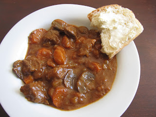 beef stew in a white bowl with a slice of bread and butter
