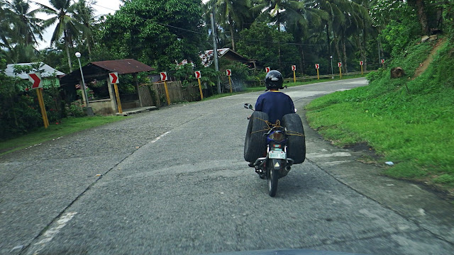 man driving a motorcycle loaded with two automobile spare tires (one on each side)